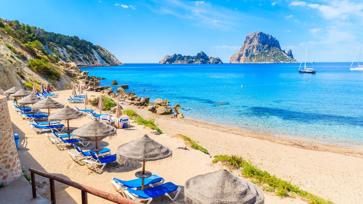 View of Cala d'Hort beach with sunbeds and umbrellas and beautiful azure blue sea water, Ibiza