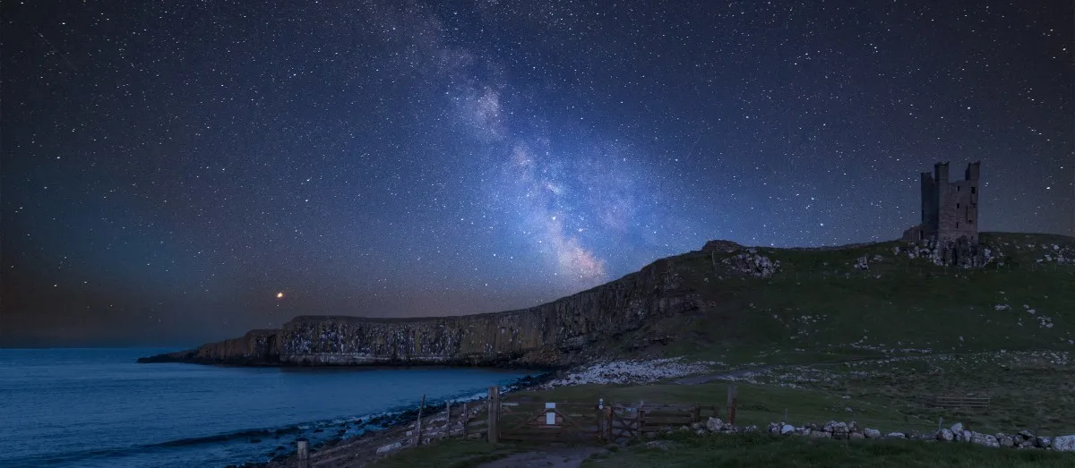 Vibrant Milky Way composite image over landscape of Dunstanburgh Castle on Northumberland coastline