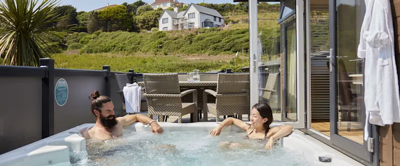 Couple relaxing in a hot tub at their lodge at Mullion Cove Coastal Retreat in Cornwall, UK