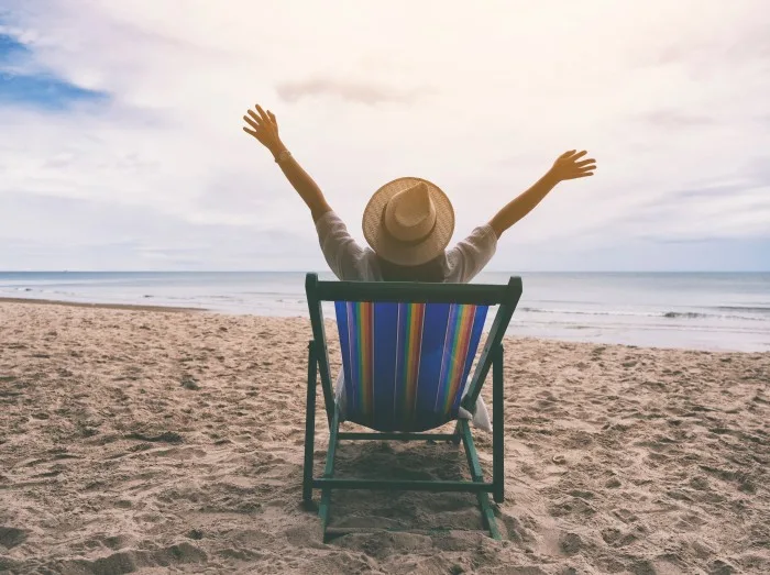 A female traveler with hat opening arms while sitting on the beach chair by the sea