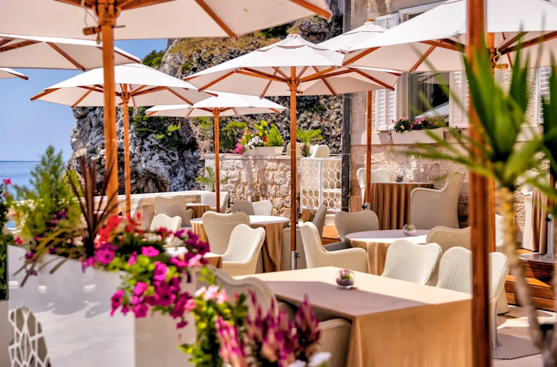 Restaurantterrasse in Dubrovnik mit Sonnenschirmen, Tischen und Stühlen in Kroatien, mit Blick auf die Adria.