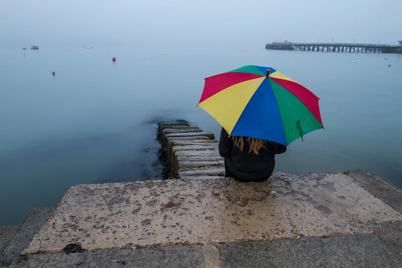 Woman sat with an umbrella looking out to sea in Swanage, Dorset, UK