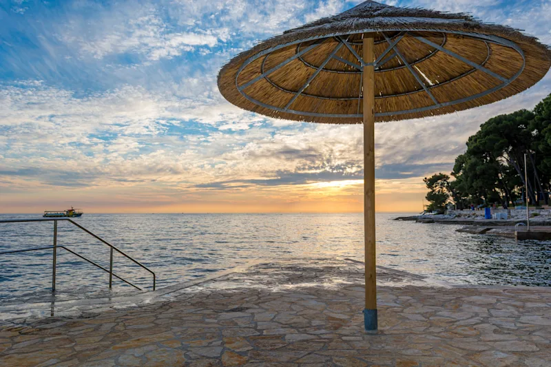 Sonnenaufgang am Meer mit Sonnenschirmen, die auf frühe Gäste warten.