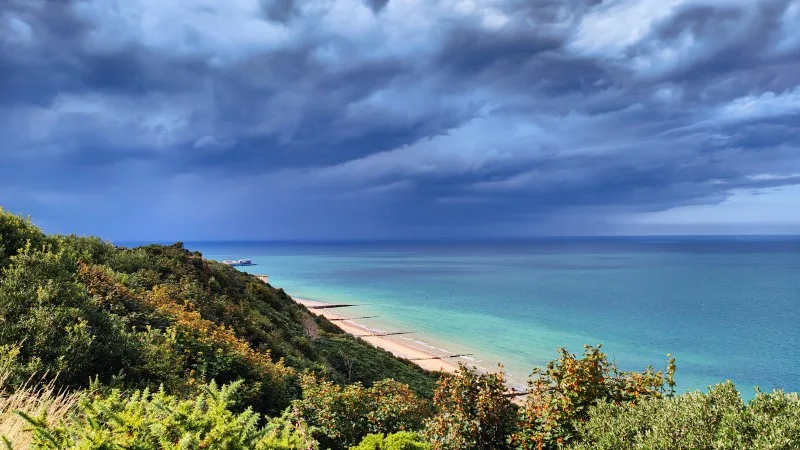 Dramatic view of the turquoise North Sea from the top of the cliffs before the storm. Sunny coastline and dark storm clouds. Cromer, Norfolk,