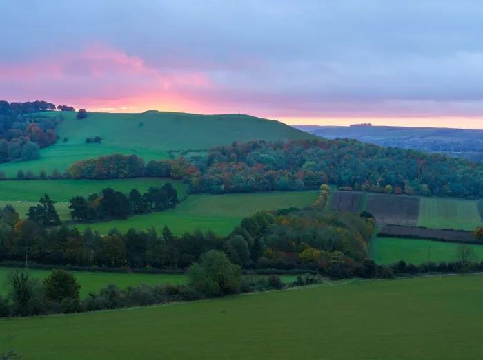 dramatic purple, red, pink and orange sky as the sun rises over Giant's Grave, Oare. View from South facing edge of the Marlborough Downs, Pewsey Vale, Wiltshire