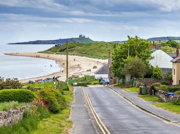 View down the hill to the sandy beach at Low Newton-by-the-Sea in Northumberland, with Dunstanburgh Castle in the distance.