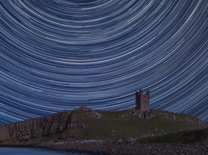 Digital composite image of star trails around Polaris with Landscape image of Medieval Castle ruins on coastline