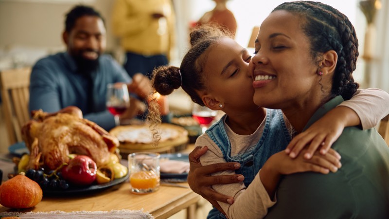 Grateful black girl kisses her mother during family meal.