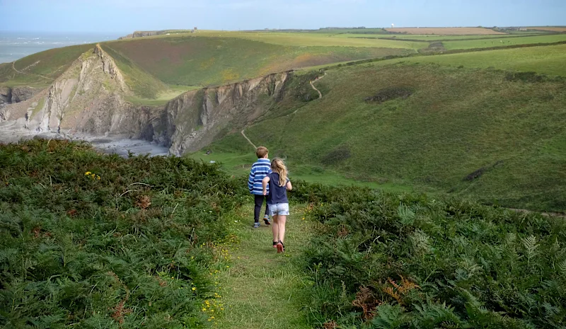 Children running along the South West Coast Path in Hartland, North Devon, UK