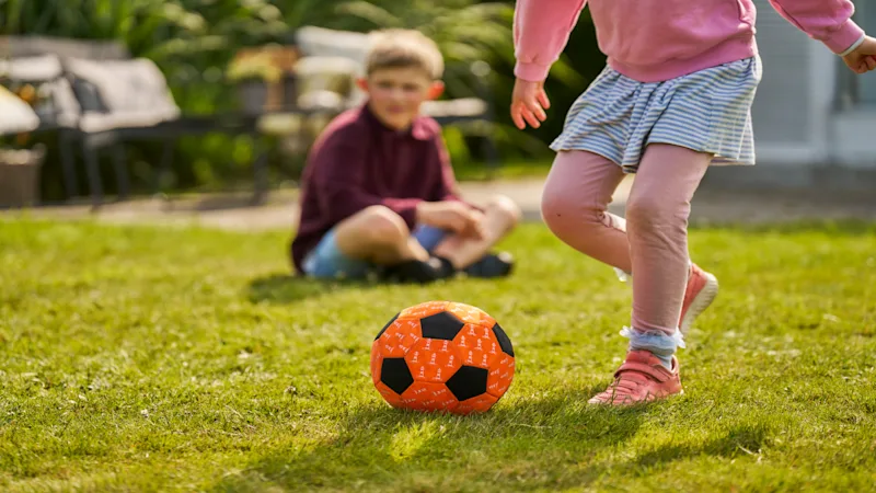 Zwei Kinder spielen mit einem Ball im Garten.