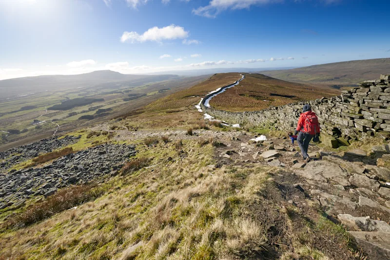 A hiker walking down from the summit of Whernside, part of the Three Peaks with Sand Beds Head Pike in the distance. The Yorkshire Dales, England, UK
