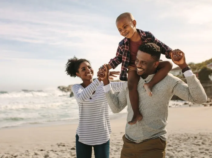 Parents carrying son on shoulders on beach vacation