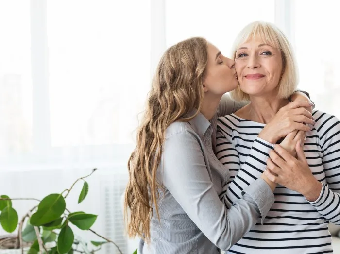 Young daughter kissing senior mother on the cheek