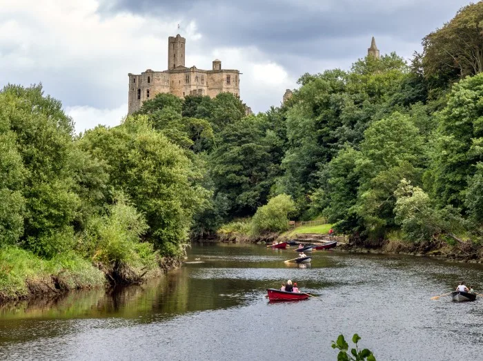 People rowing along the River Coquet by Warkworth Castle