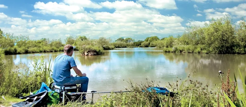 Man fishing at the onsite fishing lake at Goodiford Mill Lakes in Devon, UK