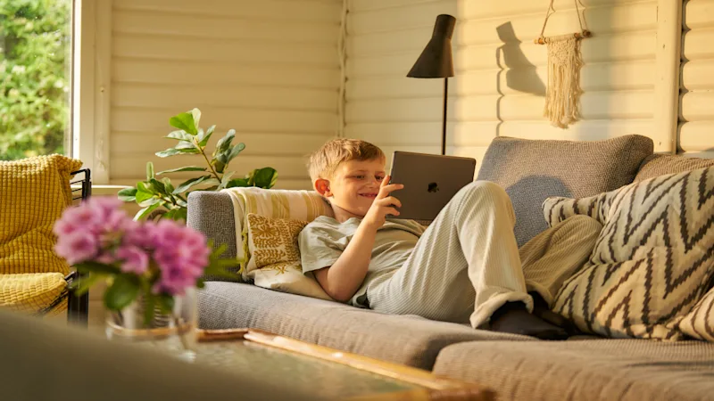 Ein Junge liegt auf dem Sofa und spielt mit seinem Tablet.