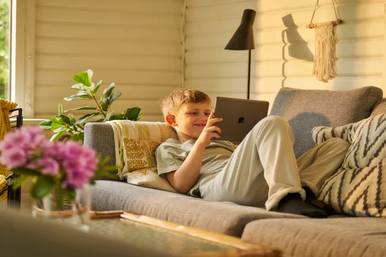 Ein Junge liegt auf dem Sofa und spielt mit seinem Tablet.