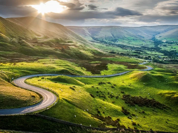 Sunset at Mam Tor, Peak District National Park, with a view along the winding road among the green hills down to Hope Valley, in Derbyshire