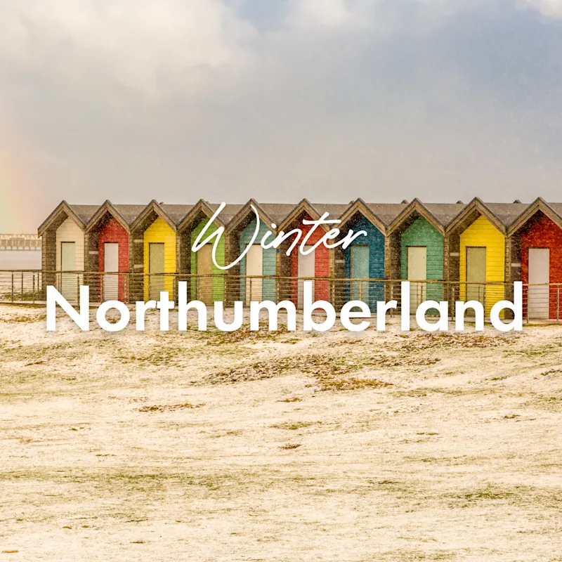 The colorful beach huts at Blyth beach surrounded by snow and with a rainbow overhead in a wintery Northumberland