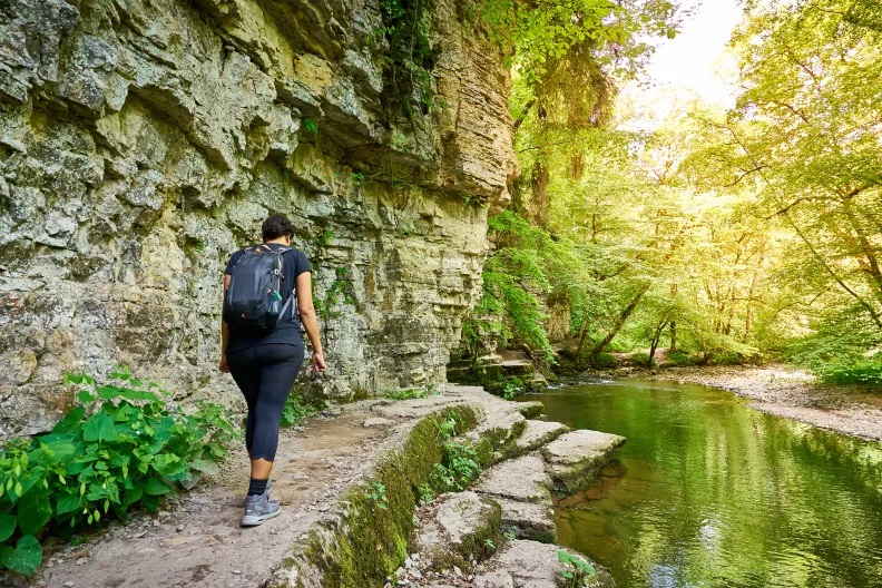 Eine Frau wandert mit Rucksack im Schwarzwald an einer Steinkante entlang.