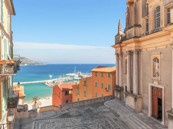 Ein kleiner Platz zwischen einer Kirche und bunten Häusern mit Blick auf das Mittelmeer in Menton, Frankreich