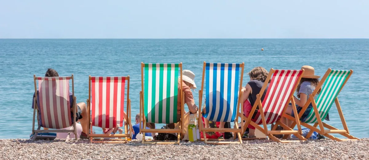 Rear View of Group of People Seated in Six Striped Deckchairs at the Seaside on a Bright Sunny Summer Day