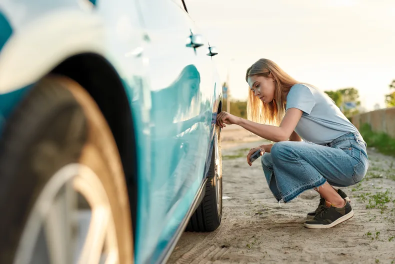 Eine Frau checkt die Reifen an ihrem Auto.