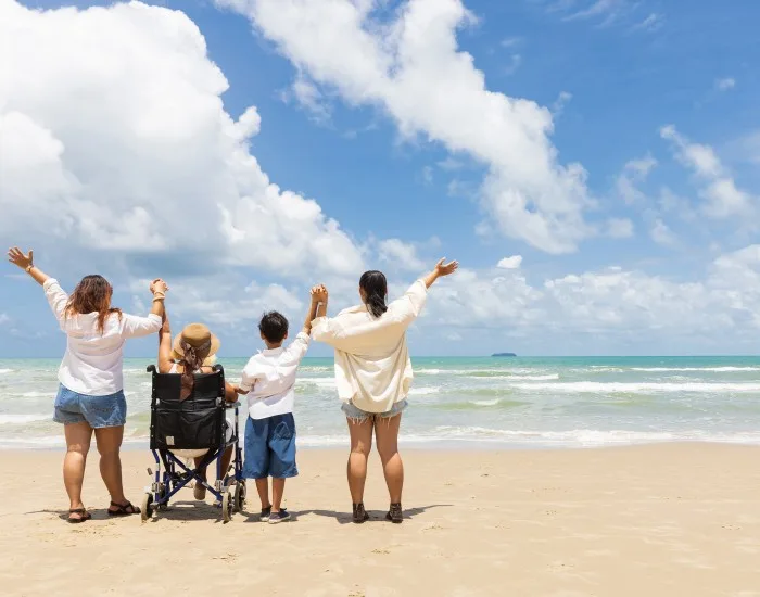 Three people standing & 1 wheelchair user having fun on the beach