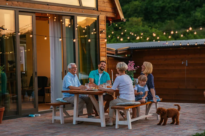 Eine Familie mit Hund genießt ein Abendessen auf der Terrasse ihres Ferienhauses.