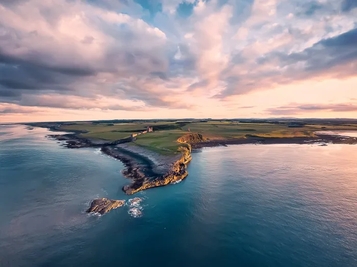 View from the air to the Embleton sea shore, North sea, the cliff with seagulls, ruins and green fields. Sunset with dramatic clouds.