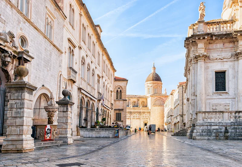 Altstadt von Dubrovnik mit weißen Steingebäuden und einer Kirche im Hintergrund.