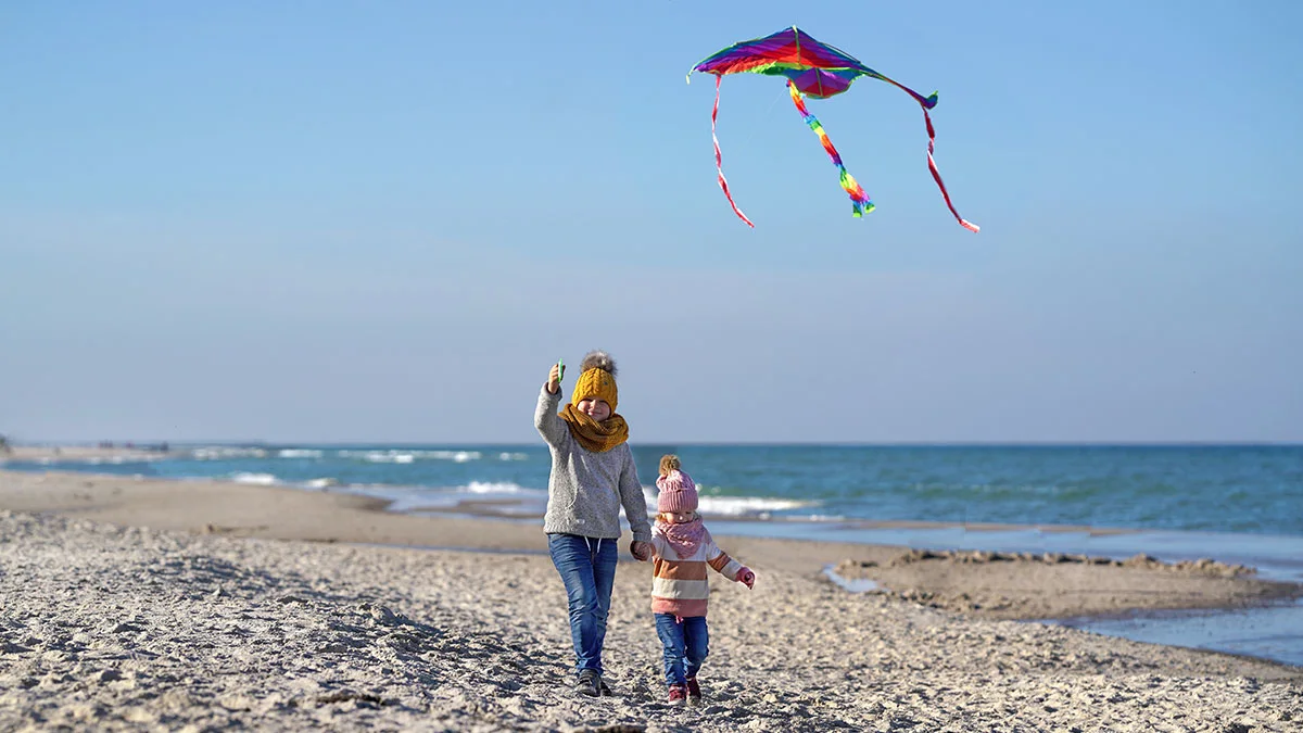 Zwei Kinder spielen am Strand im OstseeResort Olpenitz mit einem Drachen.