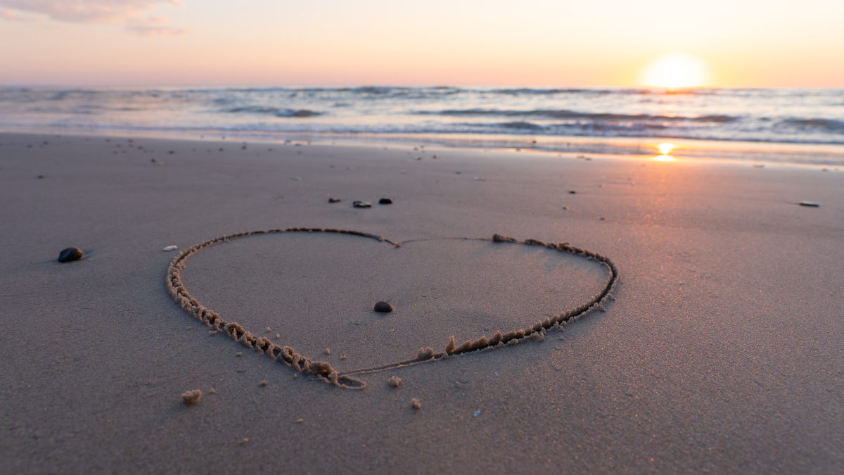 Herz am Strand mit Sonnenuntergang im Hintergrund.