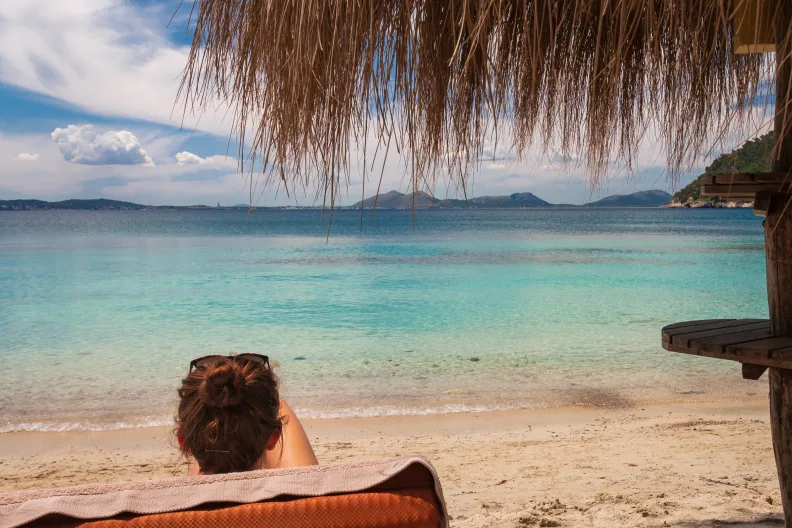 Eine Frau sitzt am Strand auf Mallorca und guckt auf das Meer.