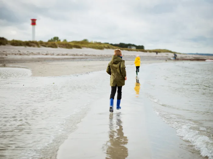 Zwei Kinder spielen in Regenkleidung am Strand.