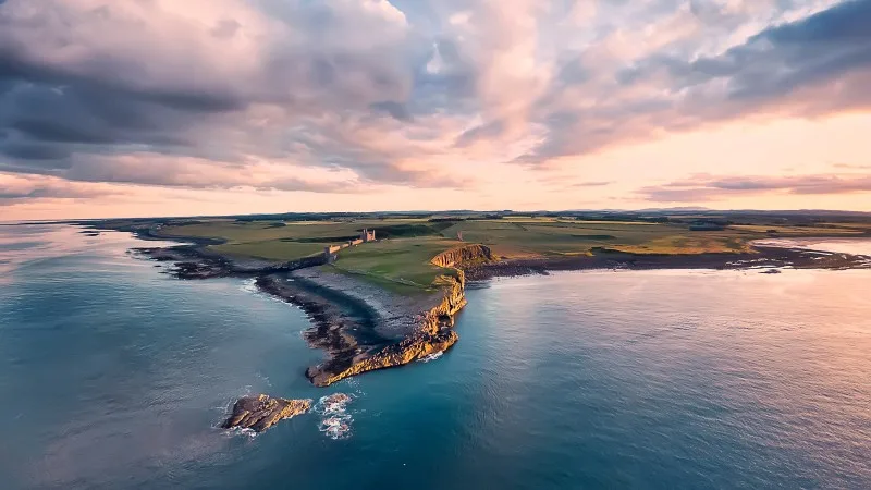 View from the air to the Embleton sea shore, North sea, the cliff with seagulls, ruins and green fields. Sunset with dramatic clouds