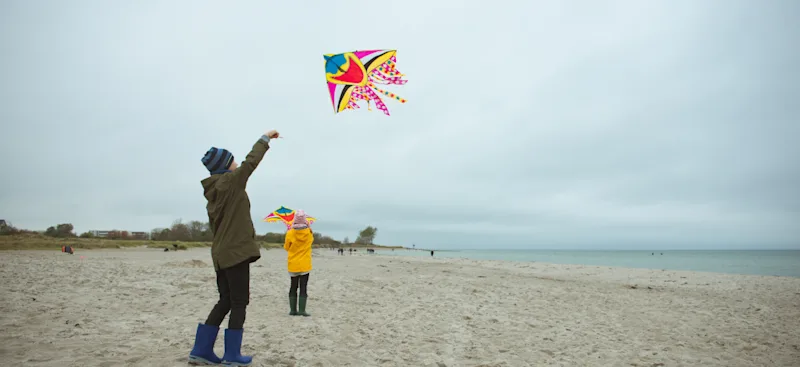 Kinder spielen am Strand mit einem Drachen im Regenwetter.