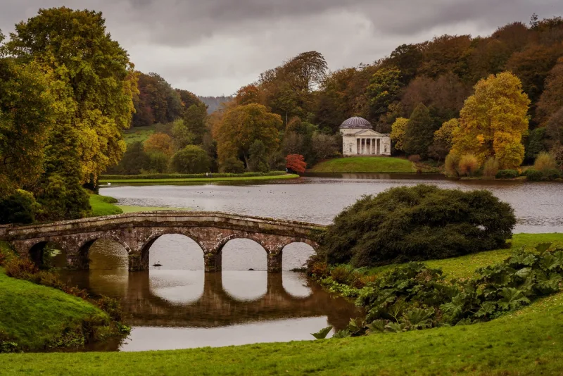 The lake and Palladian arched bridge with the pantheon temple in the distance at Stourhead Park and gardens in Warminster 