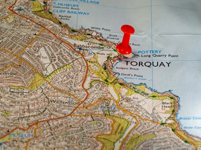 A close-up photograph of an ordnance survey map that shows the area of Torquay in Devon with a red map pin in the map at Torquay