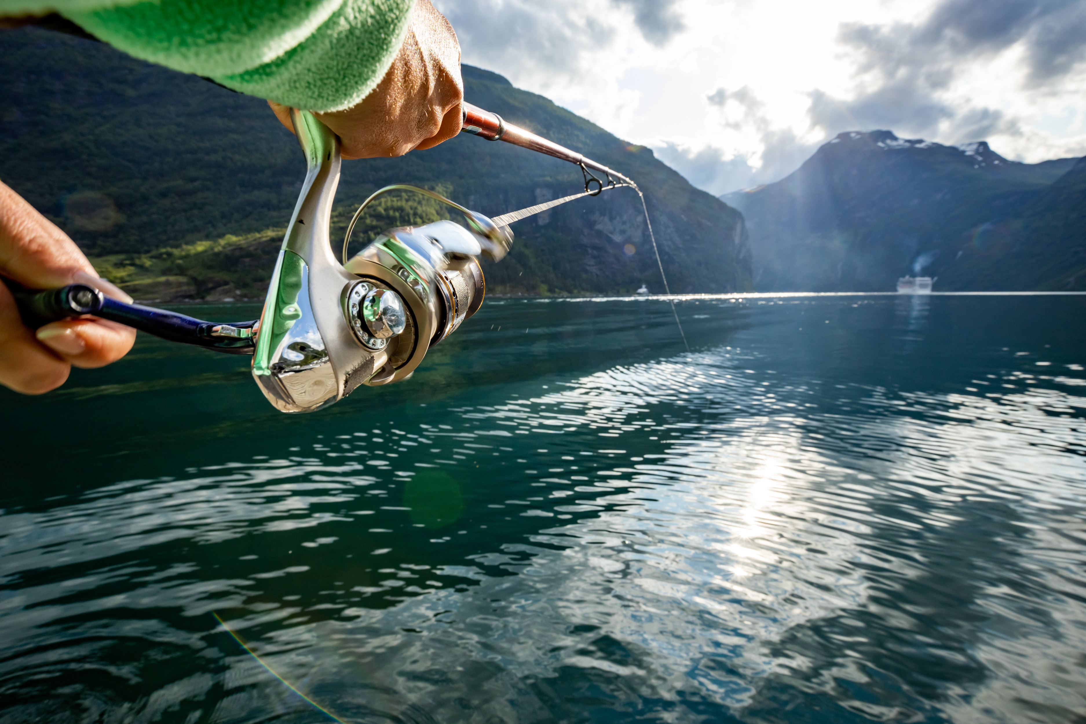 Ausgeworfene Angel mit Bergen und See im Hintergrund.