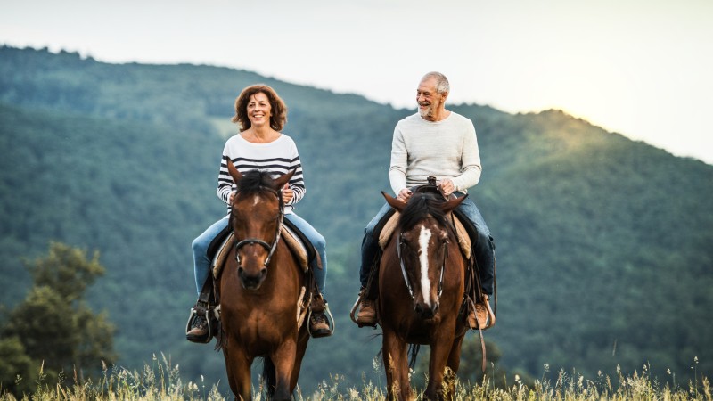 A senior couple riding horses in nature.