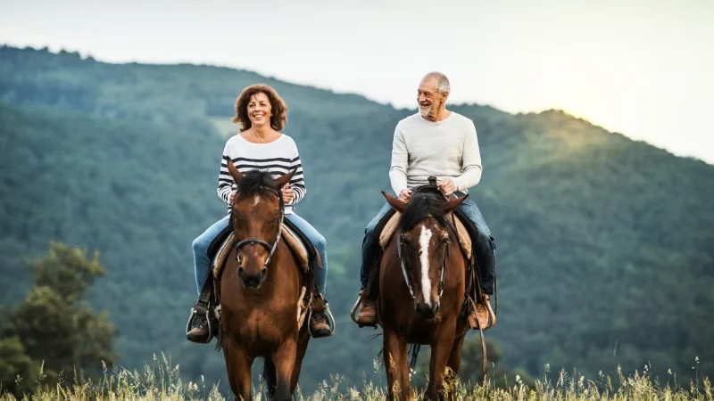 A senior couple riding horses in nature.