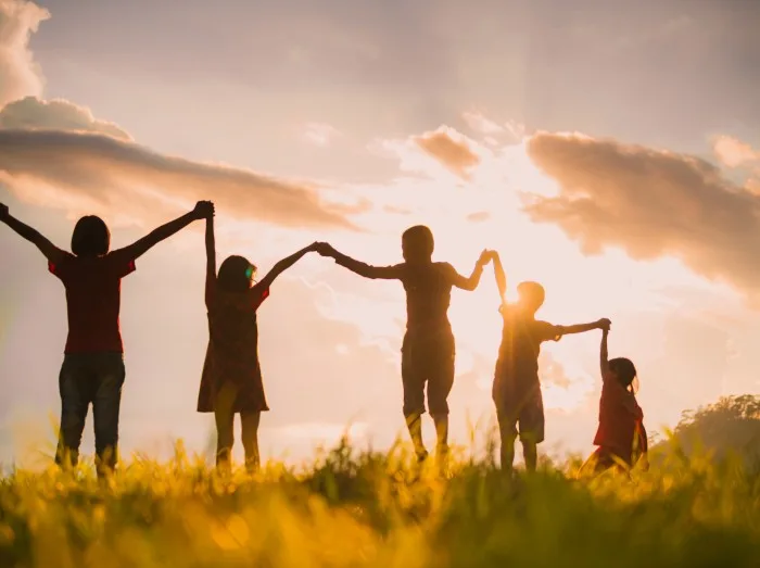 The silhouette of the children holding hands, enjoying the sunset, a group of friends cheering and arms raised in the orange sky and the mountains behind