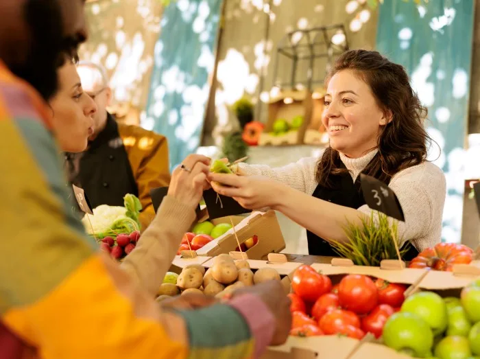 Friendly farmer offering samples to customers, showcasing homegrown fruits and vegetables at local farmers market.