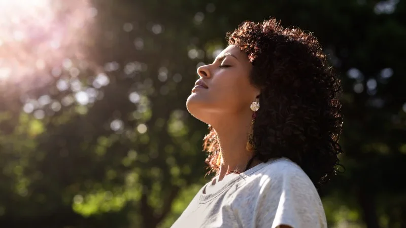 Young woman standing outdoors feeling the sun on her face