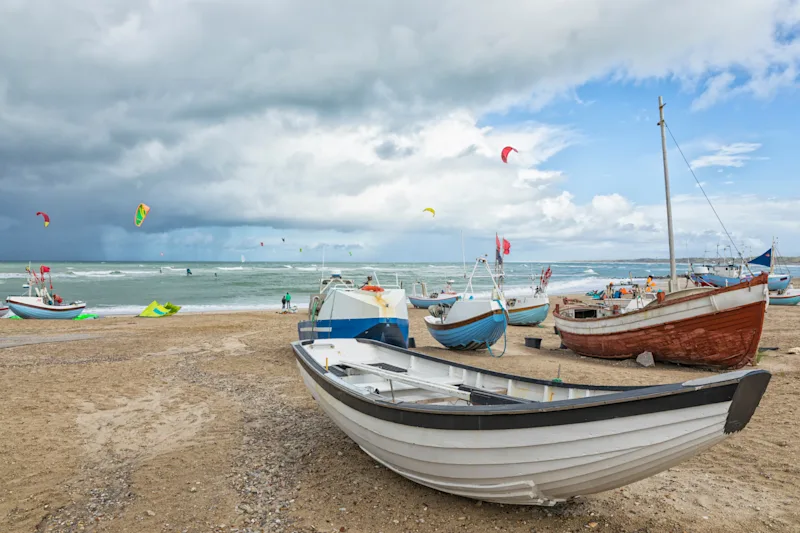 Fiskerbåde og surfere på stranden ved Nørre Vorupør i Danmark.