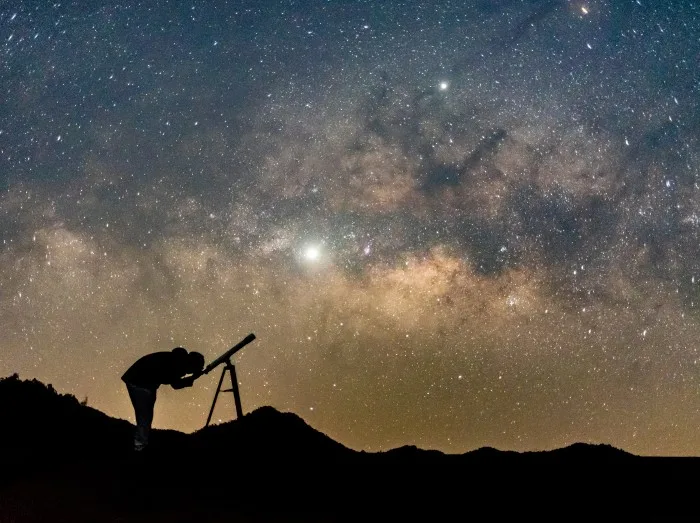 Silhouette of man watching star in telescope against milky way galaxy with stars and space dust in the universe.