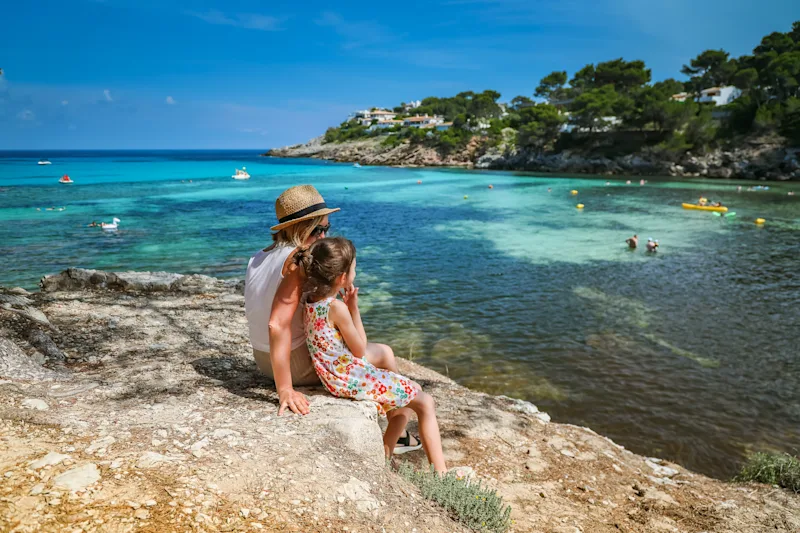 En mor og datter nyder udsigten fra klipperne på en strand på Mallorca