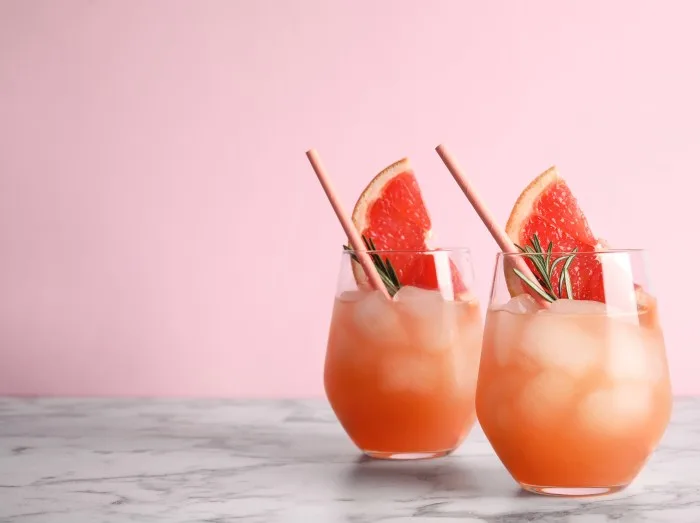 Glasses of grapefruit cocktails on table against color background.