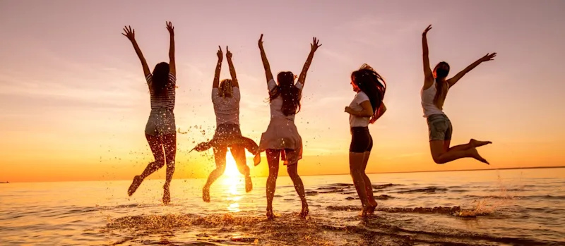 Group of happy young girls are having fun and jumping at sunset sea beach